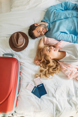 overhead view of couple of tourists lying on bed in hotel room - obrazy, fototapety, plakaty