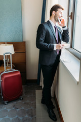 handsome businessman talking by smartphone in hotel room and looking at window