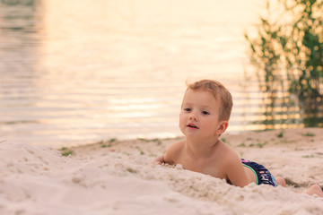 Little boy Lies on the river sand bank at sunset