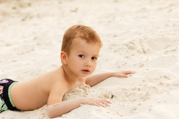 Little boy Lies on the river sand bank at sunset