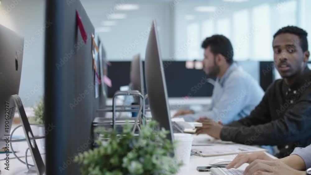 Poster tracking shot of multi-ethnic office workers working at desks in open space office, typing on modern