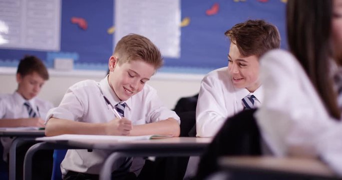 4K Happy young boys working at their desks & chatting in school classroom. Slow motion.