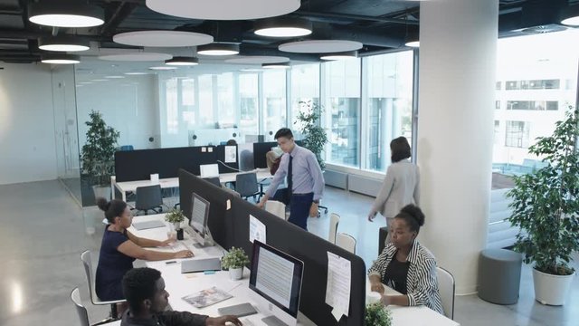 Tilt down shot of businessmen and businesswomen of different ethnicities working in modern open space office with panoramic windows