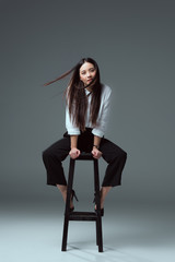 beautiful young asian woman sitting on chair and looking at camera on grey