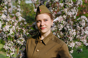 Pretty Soviet female soldier in uniform of World War II stands near flowering tree