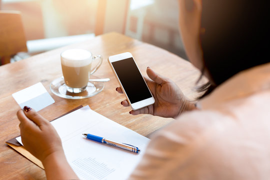 Businesswoman using cell phone with cup of coffee while working in finances