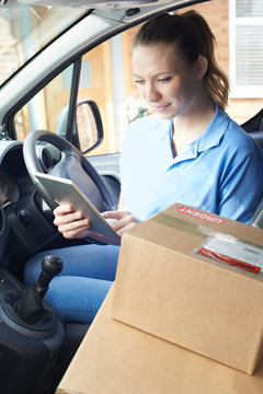 Female Courier In Van With Digital Tablet Delivering Package To House