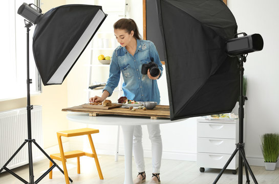 Young woman with professional camera preparing still life composition in photo studio