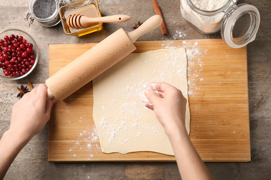 Woman scattering flour onto pastry dough on wooden board