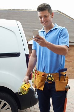 Electrician With Van Texting On Mobile Phone Outside House