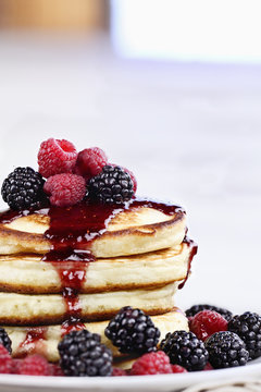 Delicious homemade golden pancakes with fresh blackberries, raspberries, and raspberry syrup. Extreme shallow depth of field.