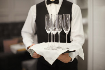 Waiter holding tray with glasses indoors, closeup