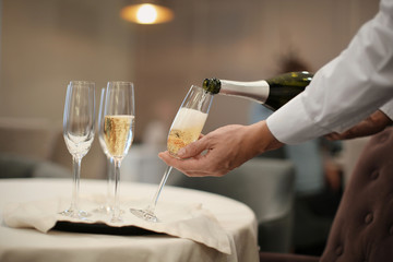 Waiter pouring champagne into glasses indoors, closeup