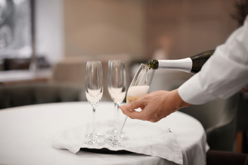 Waiter pouring champagne into glasses indoors, closeup