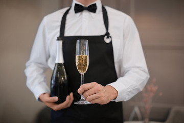 Waiter holding glass and bottle of champagne indoors, closeup