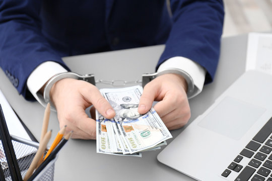 Businessman in handcuffs holding bribe at table, closeup