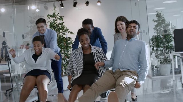 Joyous office workers pushing chairs with their excited colleagues through glass wall in modern office