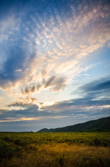 Fototapeta na wymiar Vertical sunset landscape with the sun hidden behind beautiful swirly clouds