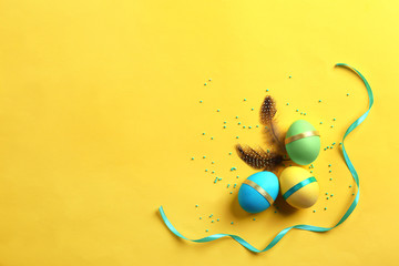 Decorated Easter eggs and feathers on color background