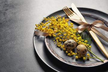 Beautiful festive Easter table setting with mimosa and eggs on gray background