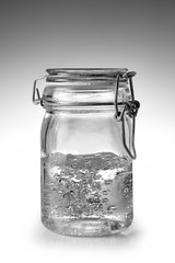 barattolo di vetro chiuso con dell'acqua su un fondo bianco sfumato a grigio