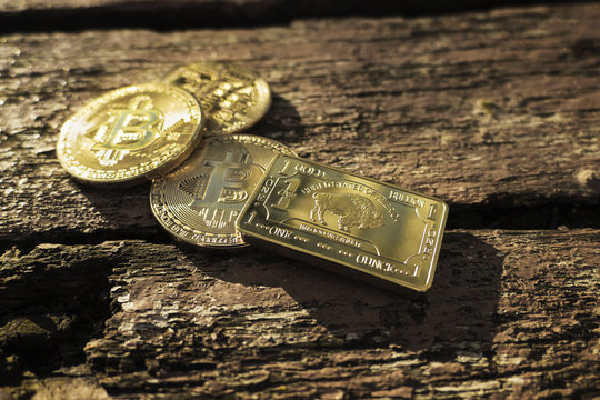 Close up photo of 3 shiny Bitcoins (BTC) and golden US ounce on wooden background with sunlight. Digital gold. Small golden brick with bitcoins. Isolated cryptocurrency in nature.