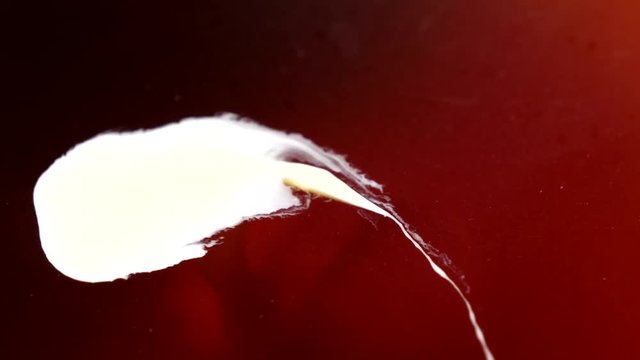 Abstract floating white blot is moving on the surface of the red / brown liquid. Dissolution of smudge. 