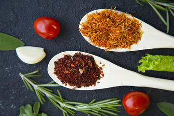 Cooking a hot spicy meal with a set of spices and herbs in wooden spoons, fresh rosemary, lettuce, garlc, and cayenne chili pepper, black concrete background, top view