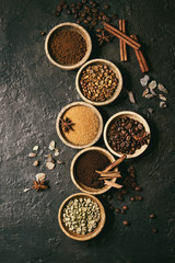 Variety of grounded, instant coffee, different coffee beans, brown sugar, spices in wooden bowls over dark texture background. Top view, space. Toned image