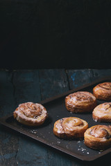 Homemade glazed puff pastry cinnamon rolls with custard and raisins on oven tray over old dark blue wooden background. Rustic style