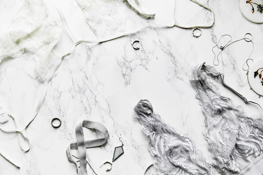 Flatlay composition with female lingerie and jewelry in monochromatic color tone on white marble background with text space.