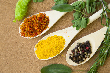 Cooking hot spicy meal. A set of spices on wooden spoons: dry salvia, pepper corns and curcuma with fresh herbs on corcwood background, top view, close up
