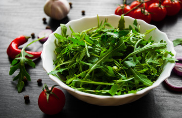 Green rucola fresh salad in white bowl on dark wooden background
