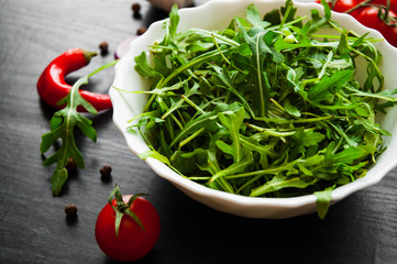 Green rucola fresh salad in white bowl on dark wooden background