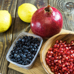 Pomegranate seeds in a wooden bowl, next to the pieces of pomegranate and a pomegranate.