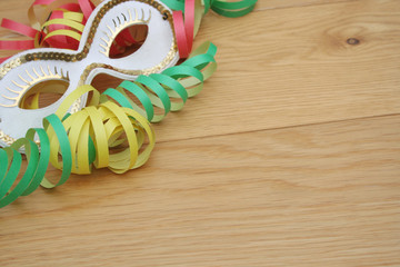 Colorful Carnival streamers and white and golden mask on wooden background