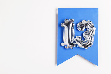 Number 13 silver balloon celebration number on a blue banner