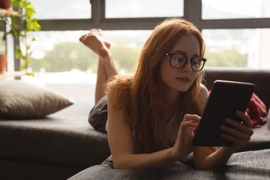 Young woman using digital tablet while lying on sofa at home