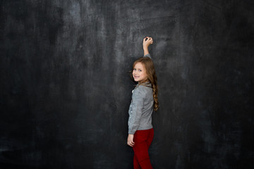Fototapeta na wymiar little girl writing something with a chalk on blackboard
