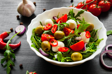 fresh salad with Green rucola, cheese, olive, tomato, onion, pepper in white bowl on dark wooden background
