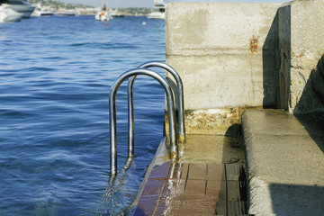 chromed iron  railing for the descent on the background of blue sea