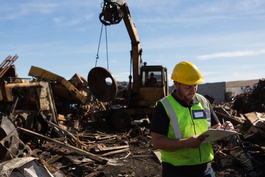 Worker writing on a clipboard in the scrapyard