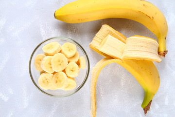 Bananas are whole and cut on a slice in a cup on a gray background.