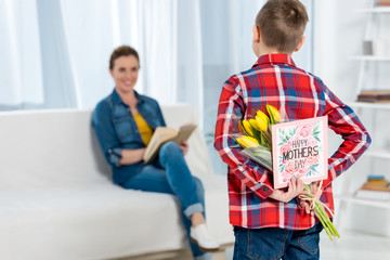 son hiding flowers and greeting card for mother behind back, mothers day concept