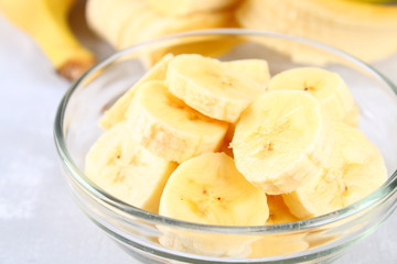 Bananas are whole and cut on a slice in a cup on a gray background.