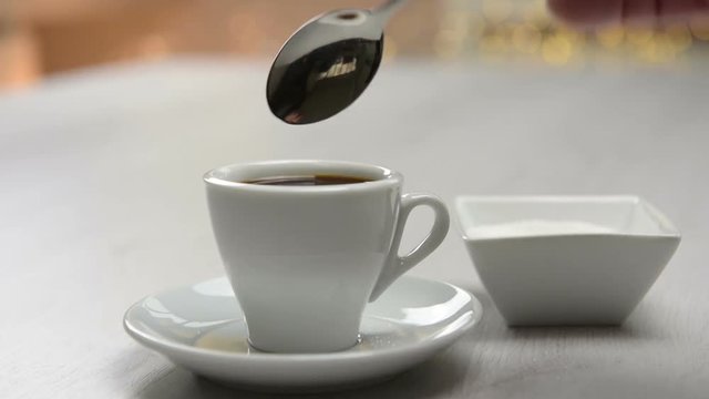pouring sugar into coffee cup on table.