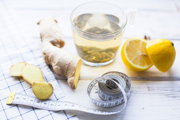 Healthy Breakfast, Sport, Fitness, Diet Concept. Tea for a weight loss with fresh lemon and ginger, white measure tape on a white wooden table with napkin