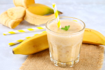Banana smoothie with a paper tube and mint. Bananas are whole and cut on a gray background.