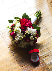 Vintage wedding bouquet with red velvet ring box on the old wooden floor. Freesia, eustoma and dark-red peony. Stylish bouquet.