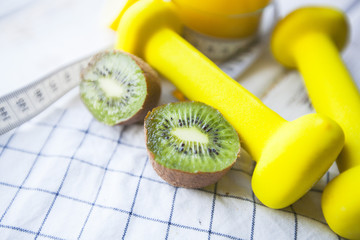 Healthy Breakfast, Sport, Fitness, Diet Concept. Fresh citrus juice, cut kiwi, yellow dumbbells and measure tape on a white wooden table with a plaid napkin